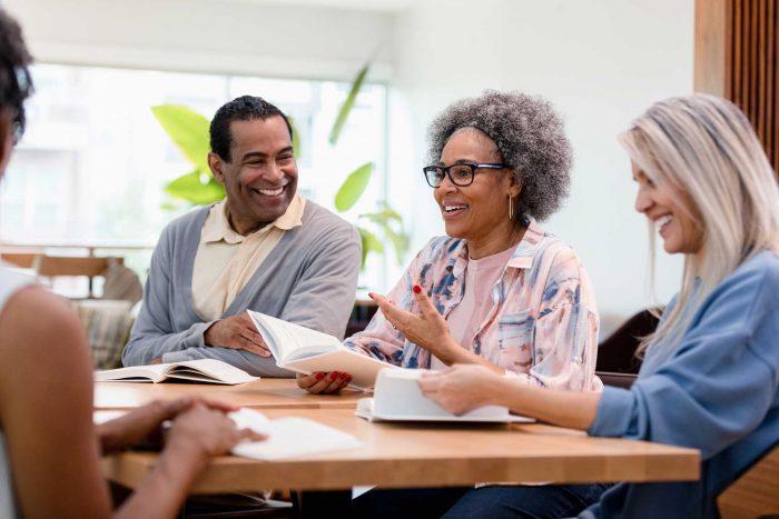 a group of seniors sitting around a table discussing a book; clubs for seniors
